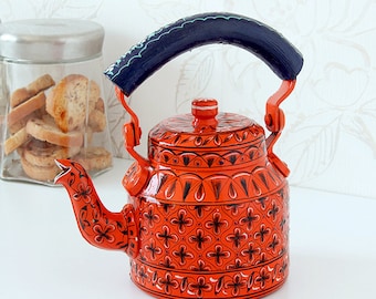 May include: A hand-painted orange kettle with a black and white floral design. The kettle has a blue handle and a spout with a floral design.