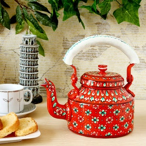 May include: A red metal teapot with a white handle and a floral design. The teapot is painted with green, white, and pink flowers.