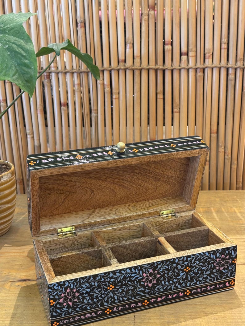 May include: A black wooden box with a floral design and a small wooden knob on the lid. The box has four compartments inside.