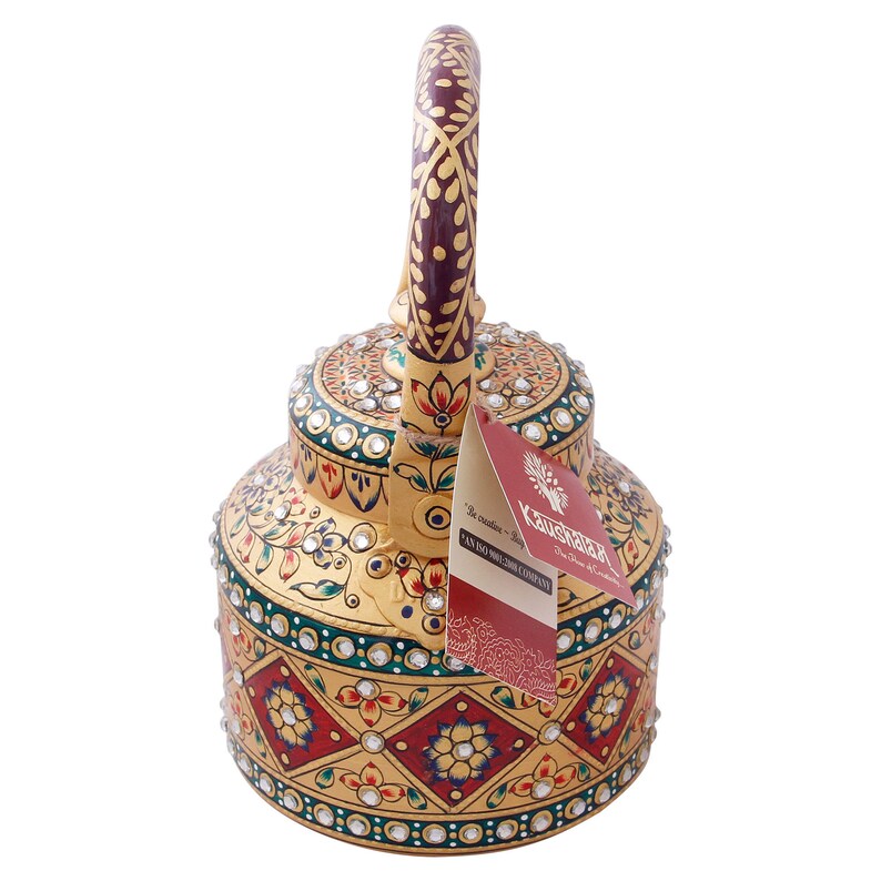 May include: A gold kettle with intricate hand-painted designs and rhinestones. The handle is maroon with gold accents. The kettle has a tag that reads "Kaushik - The Home of Art & Crafts".