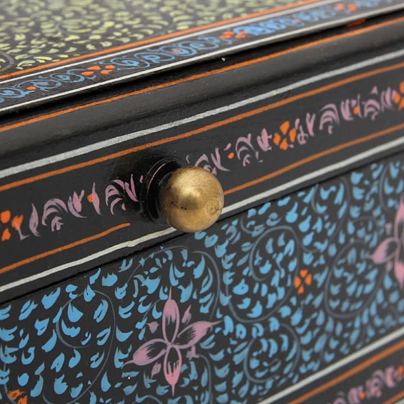 May include: A black wooden box with a brass knob. The box is decorated with intricate floral patterns in shades of blue, pink, and orange.