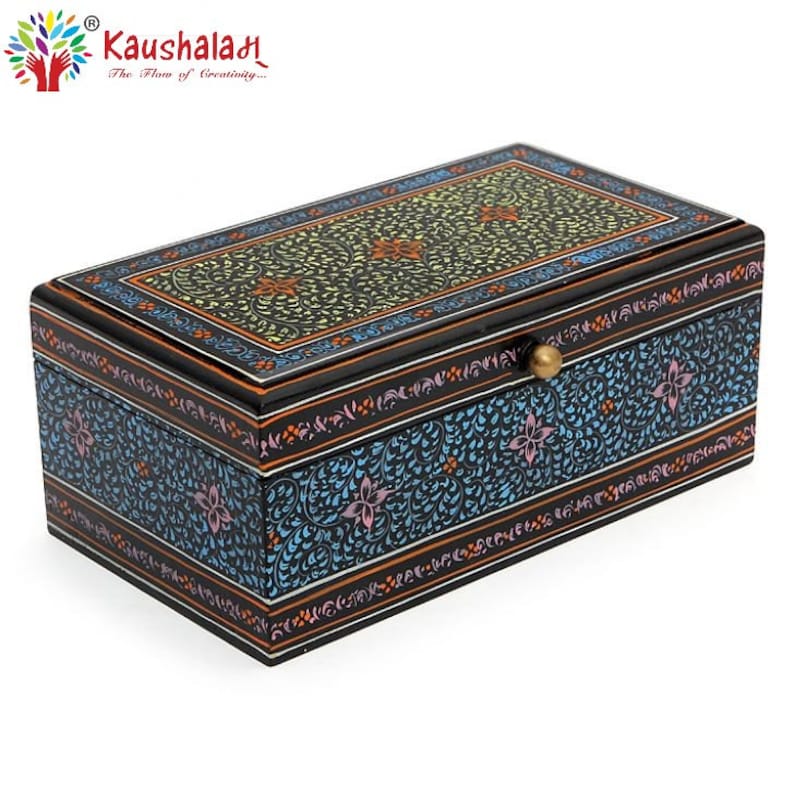 May include: A black wooden box with a floral design painted in blue, green, pink, and orange. The box has a brass knob on the lid and the words "Kaushalah The Flow of Creativity..." are printed on the top.