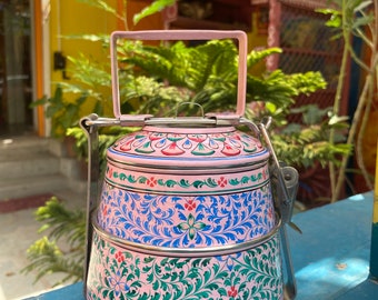 Op de afbeelding: Een roze en blauwe metalen lunchbox met een bloemenpatroon. De lunchbox heeft drie lagen en een handvat.