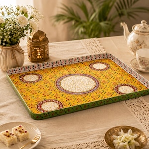 May include: A rectangular metal serving tray featuring a vibrant yellow background with a repeating floral pattern, a large central circular medallion, and three smaller circular accents, all bordered by a green rim with a decorative leaf motif.