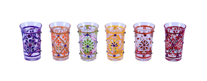 May include: A set of six clear glass shot glasses, each featuring distinct hand-painted floral and geometric patterns in vibrant colors including purple, orange, green, yellow, brown, and red, accented with small raised dots along the sides.