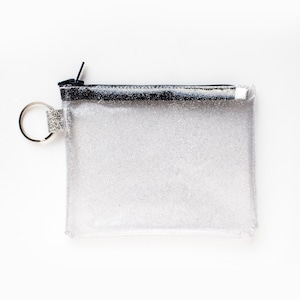 May include: A clear, rectangular glittery pouch with a black zipper and a silver key ring. The pouch is filled with silver glitter and has a black border along the top. The key ring has a small, decorative silver band.