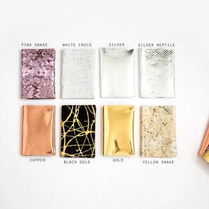 May include: A collection of eight rectangular wallets in various colors and textures. The wallets include pink snake, white croco, silver, silver reptile, copper, black gold, gold, and yellow snake. Each wallet is labeled with its respective color or pattern.