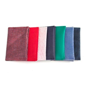 May include: A collection of colorful leather wallets in various shades, including burgundy, red, pink, navy, green, and blue. Each wallet has a unique texture or pattern, with a clean, minimalist design. The wallets are arranged in a row against a white background.