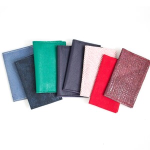 May include: A collection of eight textured wallets in various colors, including blue, green, navy, pink, red, and burgundy. The wallets are arranged in a fan shape against a white background, showcasing their different textures and hues.
