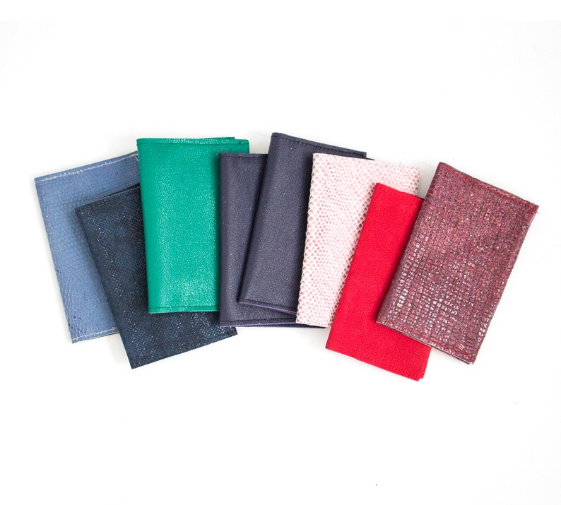 May include: A collection of eight textured wallets in various colors, including blue, green, navy, pink, red, and burgundy. The wallets are arranged in a fan shape against a white background, showcasing their different textures and hues.