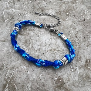 May include: Blue and white braided bracelet with silver metal accents and a lobster clasp closure.