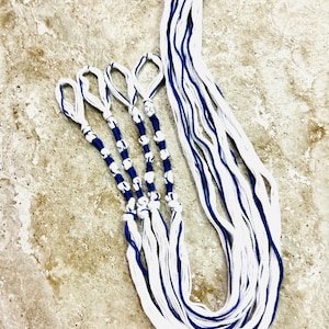May include: White and blue braided cords with blue beads, tied together in a knot at the end. The cords are arranged in a fan shape.