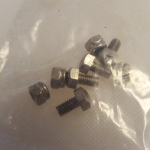 May include: A close-up of six silver metal screws with hexagonal heads and a threaded shaft. The screws are in a clear plastic bag.