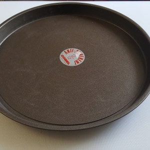 Puede incluir: Una bandeja redonda para pizza de metal gris oscuro con una pegatina roja y blanca en la parte inferior que dice "Anvil 12" en un círculo.