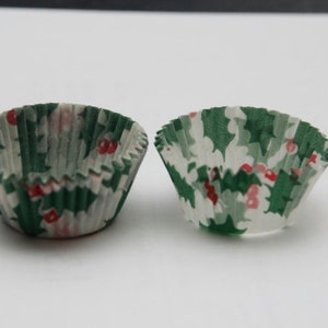 May include: Two green and white paper cupcake cases with a holly and berry pattern.