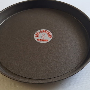 Puede incluir: Una bandeja redonda para pizza, de color gris oscuro, antiadherente con una etiqueta roja y blanca que dice "Anti-Adherente" y "GOBEL".