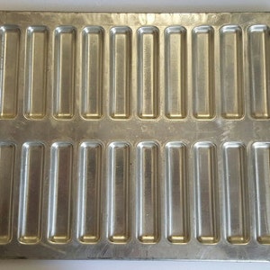 Op de afbeelding: Een zilveren bakvorm met 24 rechthoekige holtes. De vorm is ontworpen voor het bakken van kleine, rechthoekige gebakjes of koekjes.