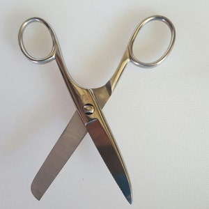 May include: A pair of silver scissors with a closed blade and an open blade. The scissors are on a white surface.
