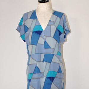 May include: A short-sleeved dress featuring a V-neckline and a geometric pattern composed of various shades of blue, including light blue, medium blue, dark blue, and bright cyan, separated by thin grey lines across the entire garment.
