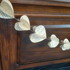 May include: A garland of paper hearts made from book pages, strung together with twine. The hearts are hanging on a dark wood surface.