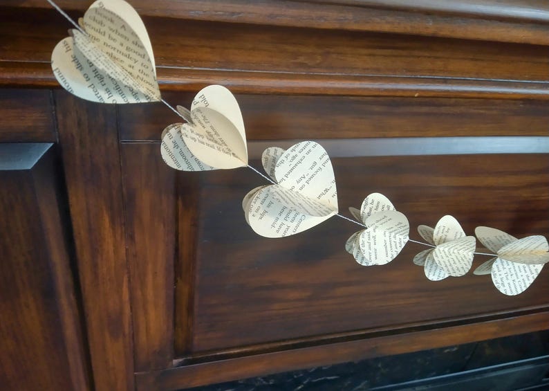May include: A garland of paper hearts made from book pages, strung together with twine. The hearts are hanging on a dark wood surface.