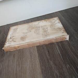 May include: A white canvas with a brown border, featuring a decorative design of handwritten script and floral elements. The canvas is lying on a wood floor.