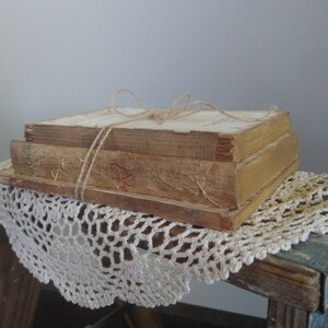 Puede incluir: Una pila de tres libros antiguos atados con cuerda, descansando sobre un encaje blanco de ganchillo en una superficie de madera.