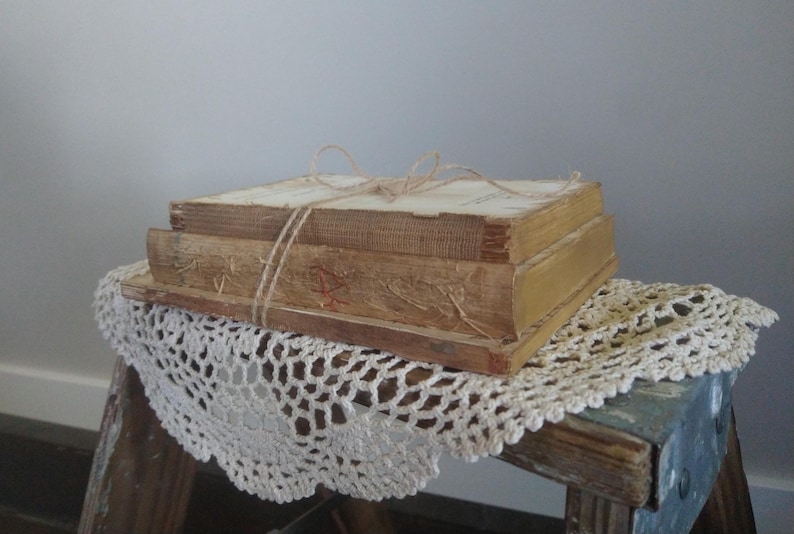 Puede incluir: Una pila de tres libros antiguos atados con cuerda, descansando sobre un encaje blanco de ganchillo en una superficie de madera.