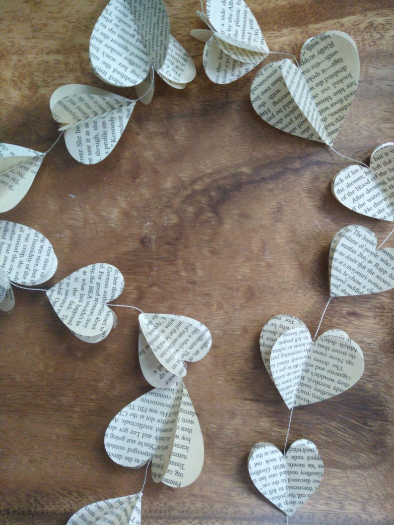 May include: A garland of paper hearts made from book pages. The hearts are strung together with white thread and are hanging on a wooden surface.