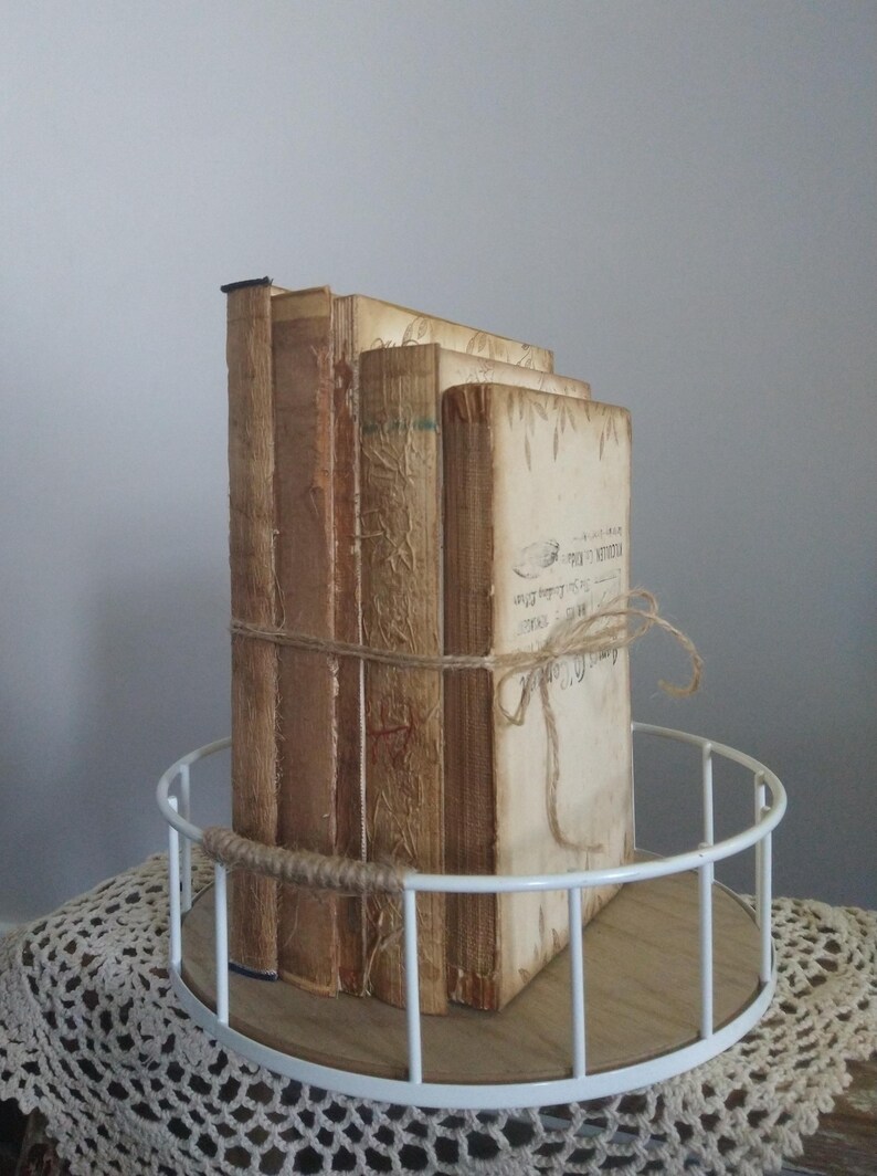 Puede incluir: Una pila de cuatro libros antiguos con cubiertas marrones y crema, atados con cuerda, sobre una bandeja de metal blanco con base de madera.