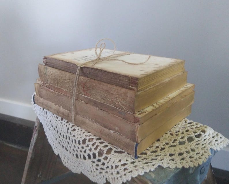 Puede incluir: Una pila de libros antiguos con cubiertas desgastadas, atados con un cordel. Los libros est&aacute;n dispuestos sobre un encaje blanco de ganchillo.