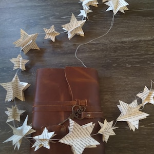 May include: A brown leather journal with a key attached to the strap. A string of paper stars hangs over the journal.