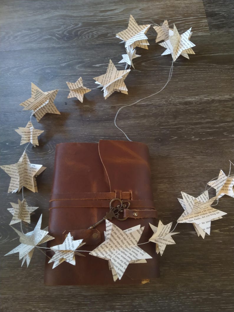 May include: A brown leather journal with a key attached to the strap. A string of paper stars hangs over the journal.