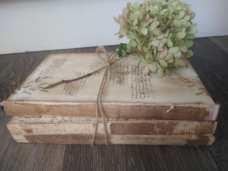May include: A stack of three vintage books with brown covers and white pages. The books are tied together with twine and decorated with dried flowers.