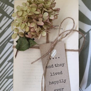 May include: A bundle of old book pages tied with twine, decorated with dried flowers and a tag. The tag says "and they lived happily ever after." The flowers are a mix of green and pink shades.