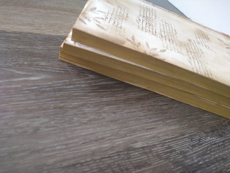 May include: Three stacked books with a cream-colored cover and a brown, patterned design. The design features a repeating pattern of leaves and lines.