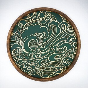 May include: A round wooden tray with a green background and a gold wave pattern. The tray is ideal for serving snacks or drinks.