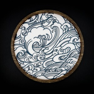 May include: A round wooden coaster featuring a blue and white wave design. The coaster is ideal for protecting surfaces from scratches and spills.