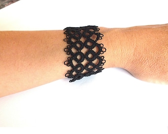 Puede incluir: Pulsera calada negra con un patrón geométrico repetitivo. La pulsera está hecha de un material delicado, tejido a ganchillo y se abrocha con un cierre plateado. La pulsera mide aproximadamente 5 cm de ancho.