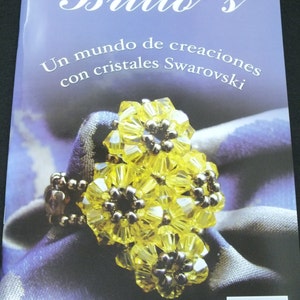 May include: A magazine cover with the title "Brillo's" and the text "Un mundo de creaciones con cristales Swarovski." The cover features a yellow crystal flower ring. The magazine is on a purple background.