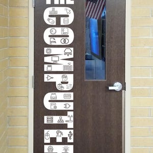 May include: A brown door with white text and icons that reads "THE COMPUTER LAB." The door has a small window with an American flag visible. The text includes computer-related symbols and terms.