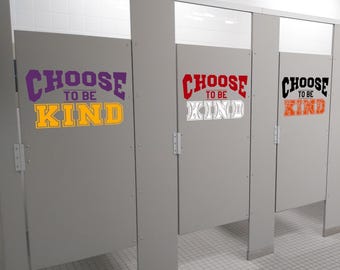 May include: Three gray restroom stall doors featuring the text CHOOSE TO BE KIND in different color combinations. The first door has purple and yellow text, the second has red and white text, and the third has black and orange text.