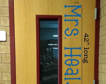 May include: A light wood-grain door with a dark red frame, a central rectangular window with diagonal wire mesh, and a silver lever handle. A blue vinyl decal reads "Mrs. Healy" vertically, accompanied by the text "42" long" next to a line.