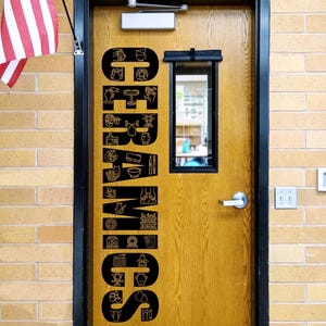 May include: A wooden door with a black metal frame and a silver handle, featuring a large vertical black decal that spells CERAMICS. The letters are filled with white line-art icons depicting pottery tools, kilns, and various ceramic vessels.