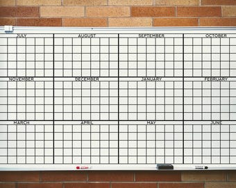 May include: A large white dry-erase whiteboard featuring a printed annual calendar grid. The board is divided into twelve sections, each labelled with a month from July to June, containing rows and columns for daily planning and scheduling.