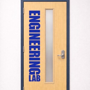 May include: A light wood-toned door with a dark blue frame, featuring a vertical rectangular frosted glass window, a silver metal lever handle, and a silver kick plate. The text "ENGINEERING LAB" is printed in bold blue capital letters.