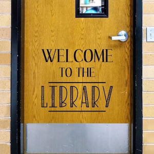 May include: A wooden door with a black metal handle and a rectangular window at the top. The door features black vinyl lettering that reads "WELCOME TO THE LIBRARY" with horizontal lines above and below the word library. A silver kick plate is at the base.