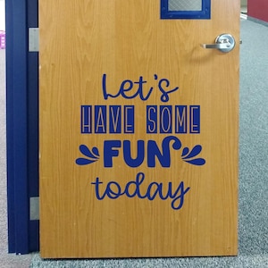 May include: A light brown wooden door featuring a dark blue vinyl decal with the text Let's HAVE SOME FUN today. The door includes a silver metal handle and a small rectangular window at the top. The text uses a mix of script and block fonts.