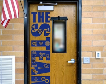 May include: A wooden door with a black frame featuring blue vinyl lettering that reads THE STEAM LAB, decorated with various icons representing science, technology, engineering, arts, and mathematics. An American flag is mounted to the left.