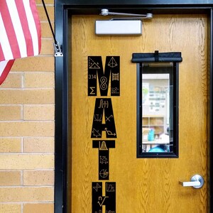 May include: A wooden door with the word "MATH" spelled out in black, geometric symbols and numbers. An American flag hangs on the left. The door has a small window and a silver handle.